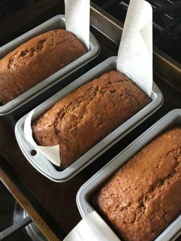 Three loaves of Small Loaf Pan Banana Bread lined with mini strips of parchment.