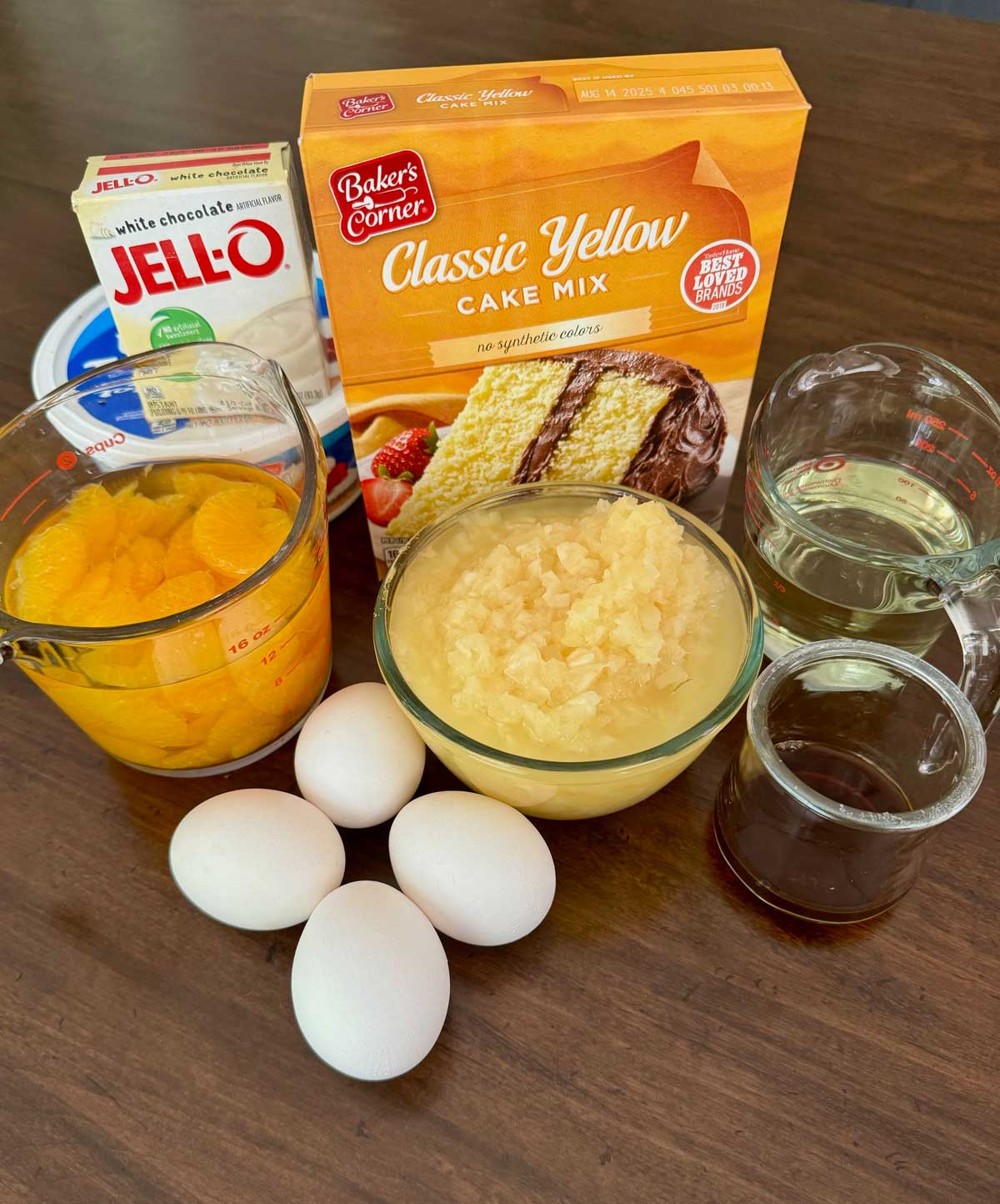 Ingredients for Pig Pickin' Cake including pudding mix, yellow cake mix, mandarin oranges, eggs, oil, pineapple, vanilla and whipped topping.