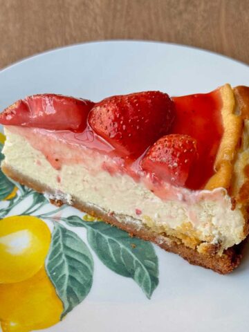 Slice of keto cheesecake with strawberry topping on a plate with lemons.